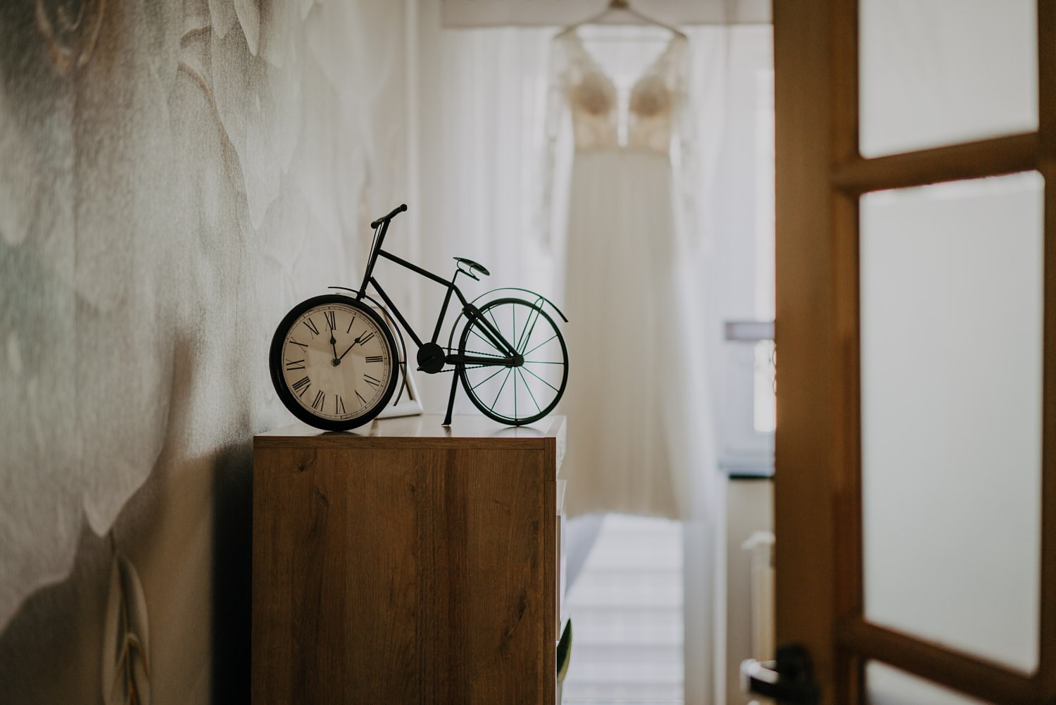 Dekoracyjny rower-zegar i suknia ślubna w tle.
